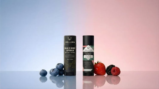 Vellora Blue E-Berry Lip Balm and Strawberry Lip Balm displayed with fresh berries on a pastel background, hydrating tinted lip care products