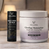 VELLORA Glowbae Moisturizer jar with ceramides, hyaluronic acid and chia placed beside VELLORA Blue E-Berry Lip Balm, showcasing a hydrating skincare and lip care combo for smooth, nourished skin and soft lips.