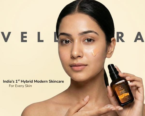 Model holding a Vellora face serum bottle with a visible serum drop on glowing skin, showcasing India’s first hybrid modern skincare brand for all skin types.